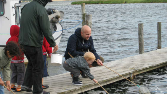 Far og søn fisker med net fra badebro